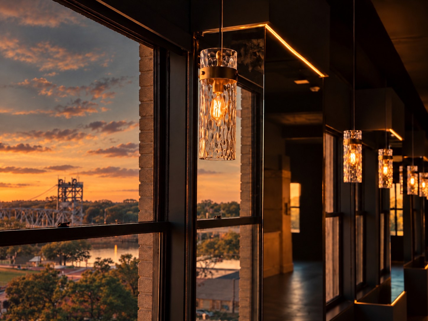 Sunset over the Red River and bridge seen through the windows of The City Club of Alexandria, with warm pendant lights